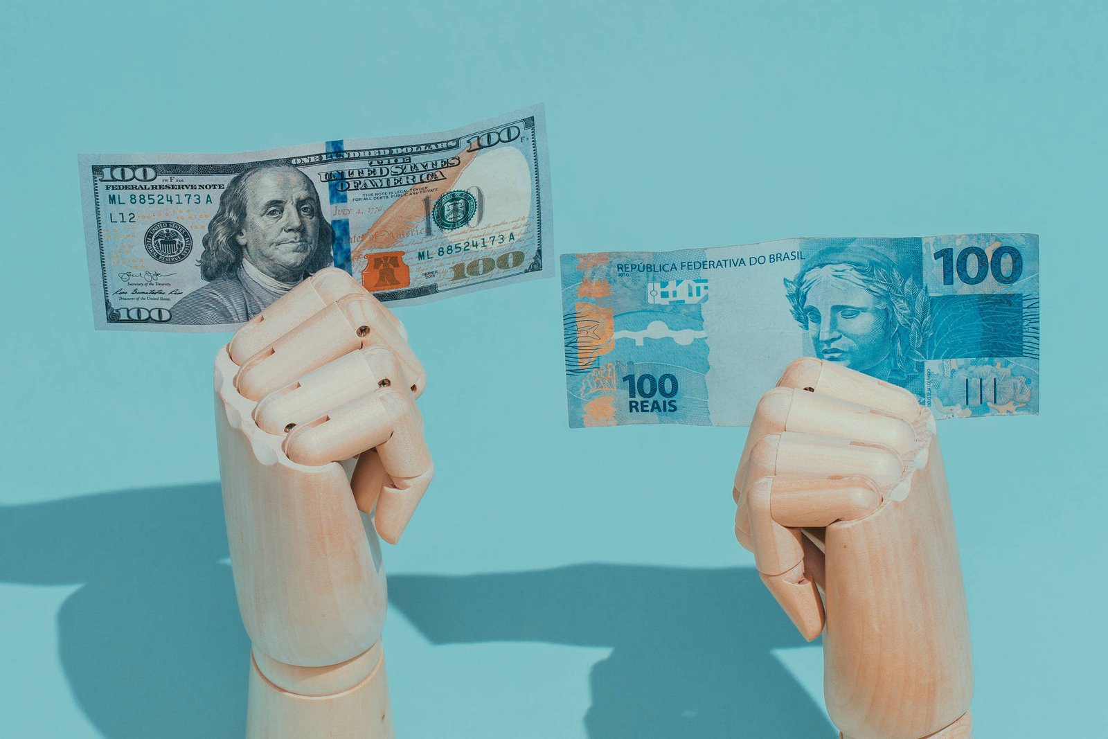 Cédulas de dólar e real seguradas por mãos de manequim