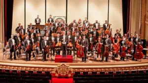 Orquestra sinfônica reunida no palco de um teatro histórico, com músicos e maestro em formação clássica, simbolizando a força da música como expressão do Espírito do Natal e da comunhão humana.