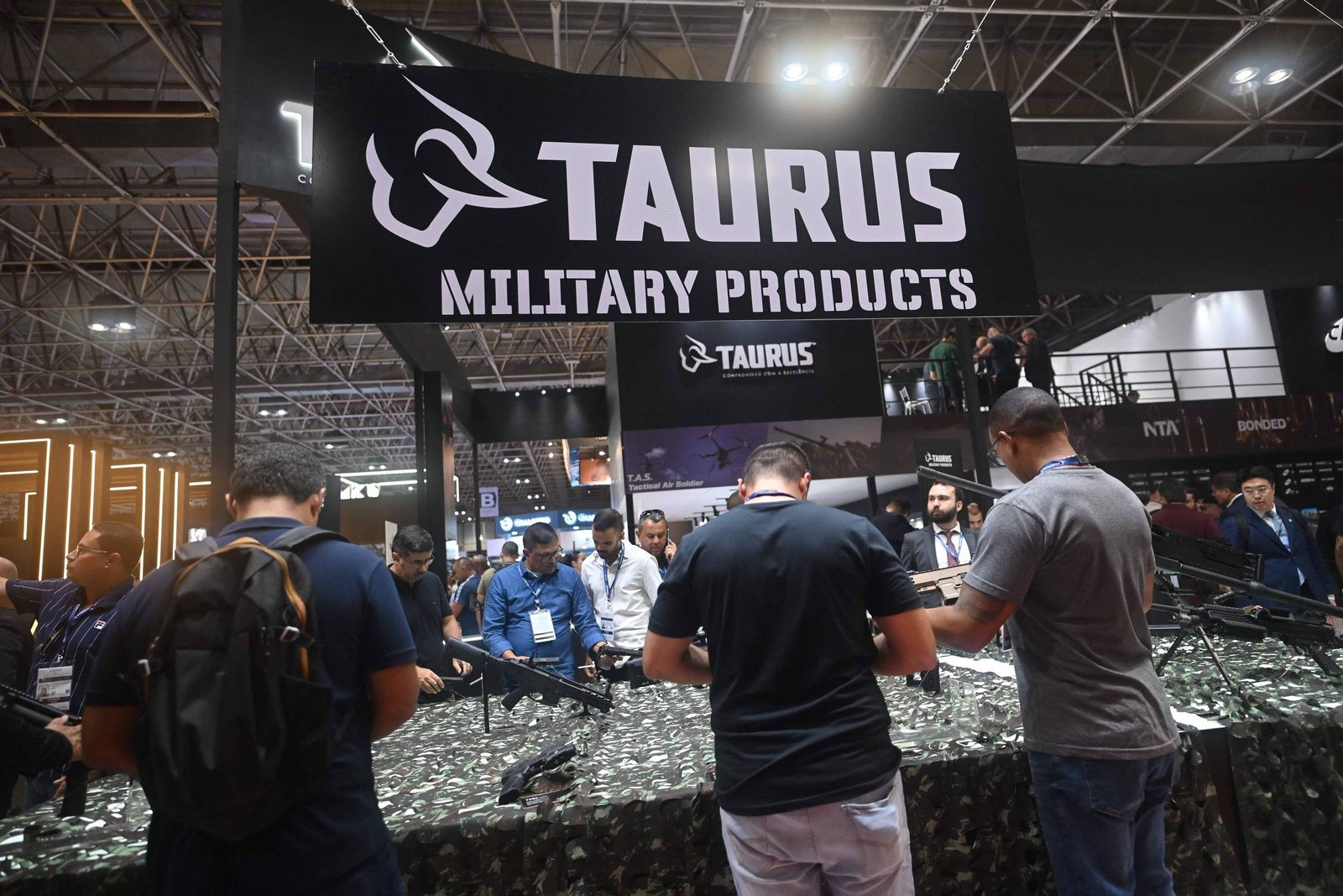 A imagem mostra um estande da Taurus, com uma grande faixa escrita