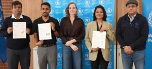 Cinco indivíduos estão de pé em frente a um cenário do Programa Mundial de Alimentos, segurando certificados, celebrando como vencedores do hackathon.