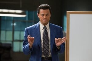 Leonardo-DiCaprio-em-O-Lobo-de-Wall-Street-2013-cena-do-filme-com-terno-azul-em-reunião-corporativa-sobre-mercado-financeiro-e-corrupção