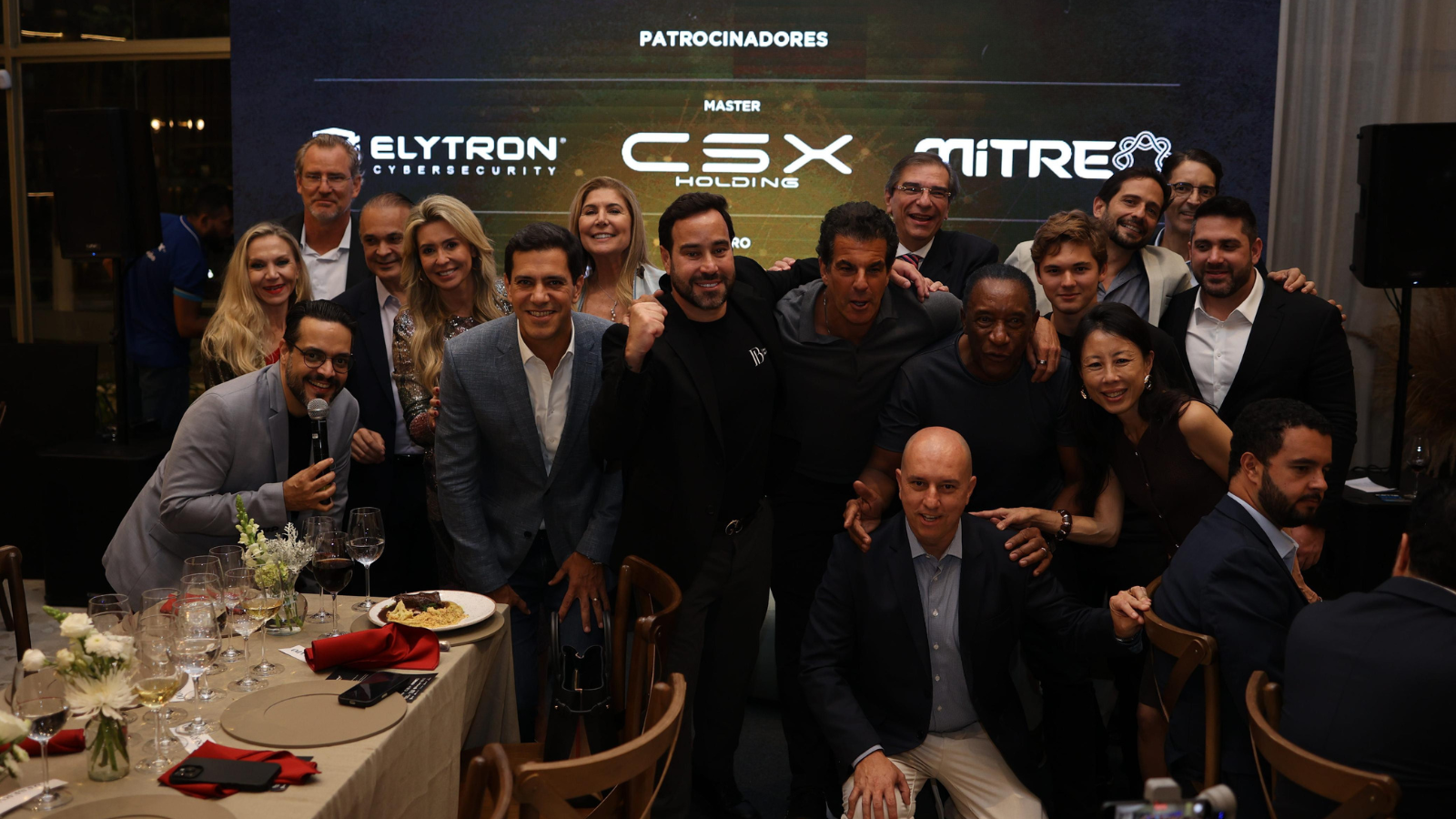 Grupo de empresários, autoridades e participantes reunidos durante jantar do Protagonistas do Brasil, em ambiente corporativo, com destaque para os patrocinadores exibidos ao fundo e interação entre lideranças.