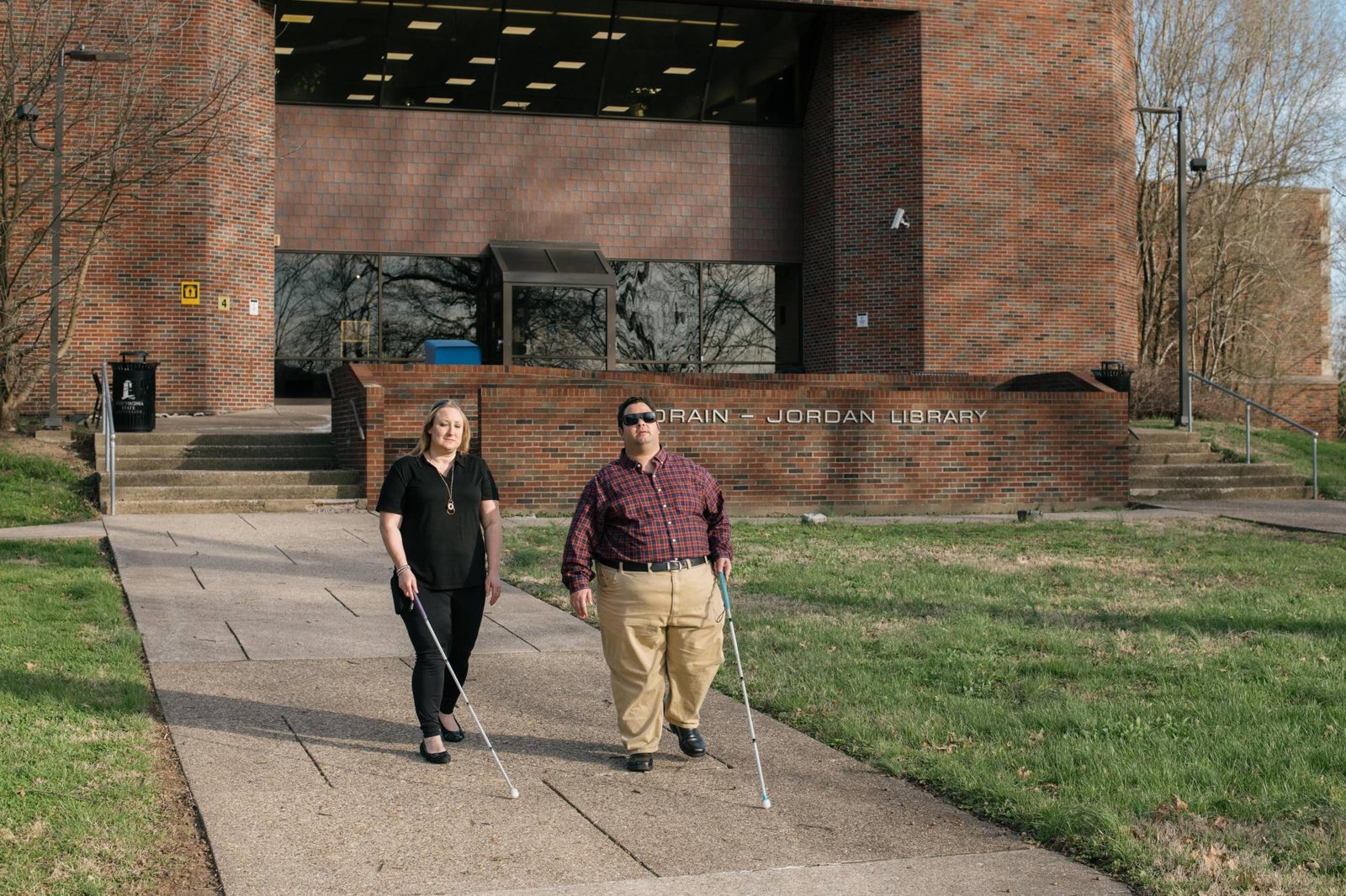 Two people who are blind are walking on the campus of West Virginia State University while holding canes.