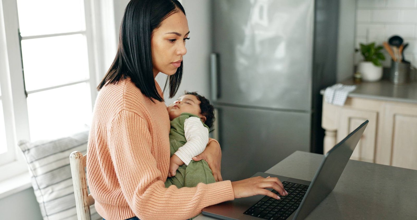 Mother, baby and laptop in kitchen for remote work.