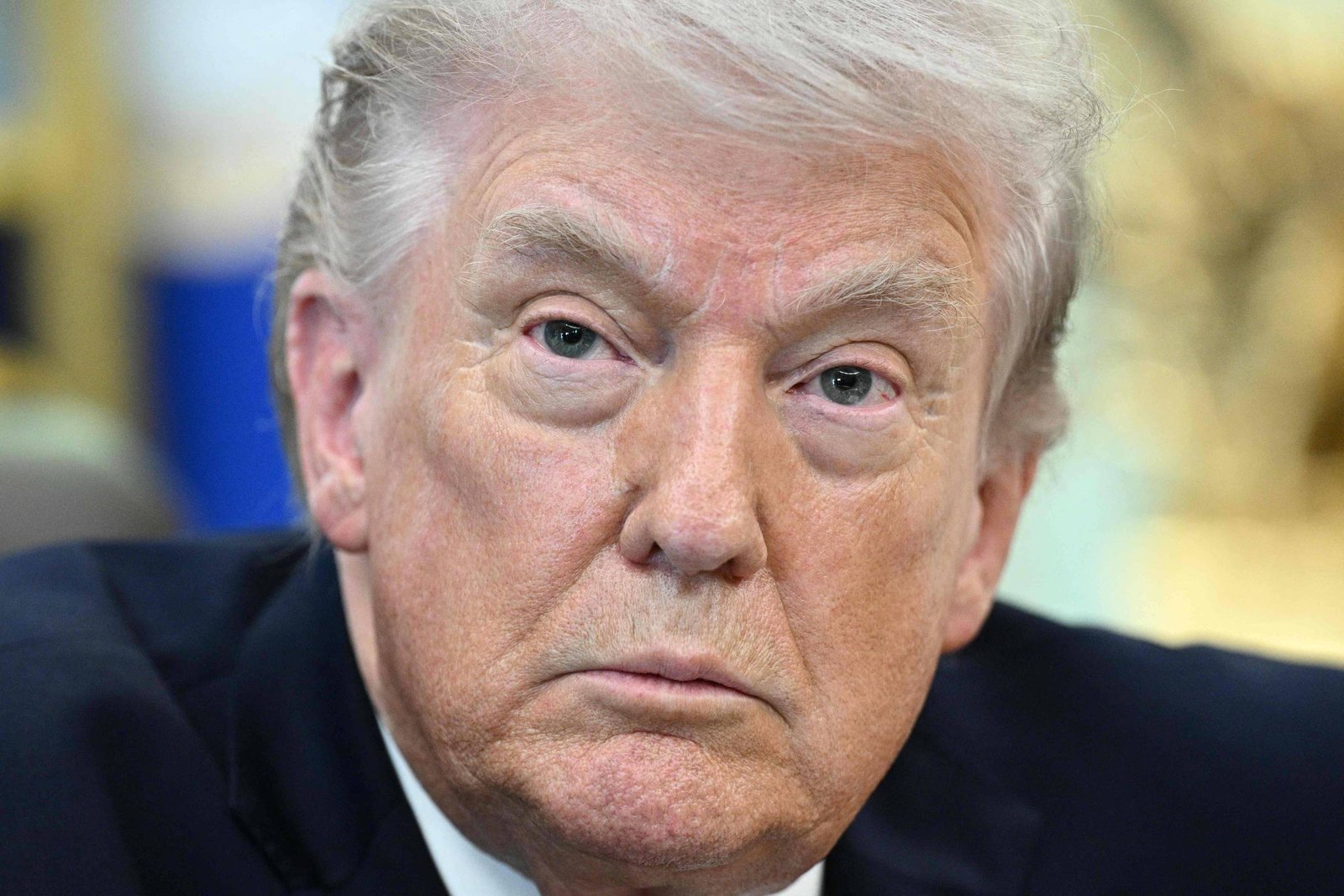 Homem branco de cabelos grisalhos penteados para trás, com expressão séria, veste terno escuro e camisa branca. Fundo desfocado em tons claros.