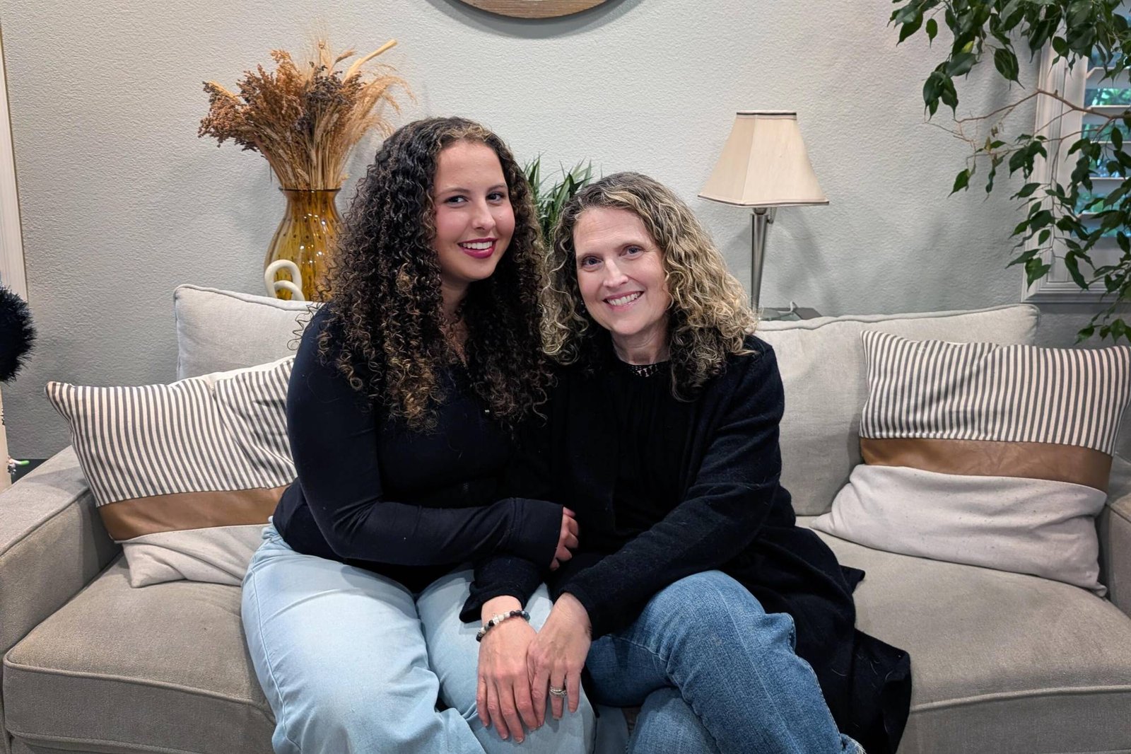 A teenager with curly, brown hair sits next to her mother.