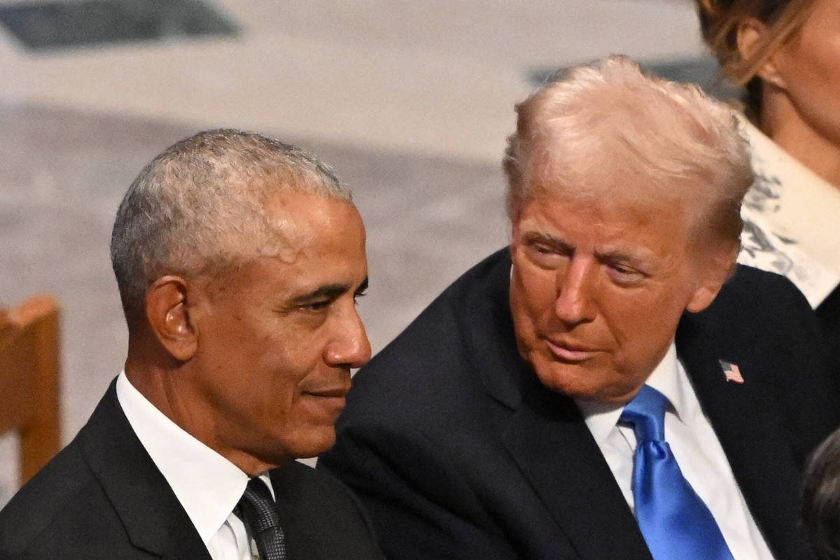 Dois ex-presidentes dos Estados Unidos sentados lado a lado em evento formal. Um deles usa terno preto com gravata preta e camisa branca, o outro veste terno preto com gravata azul e camisa branca. Ambos estão olhando um para o outro em conversa próxima.