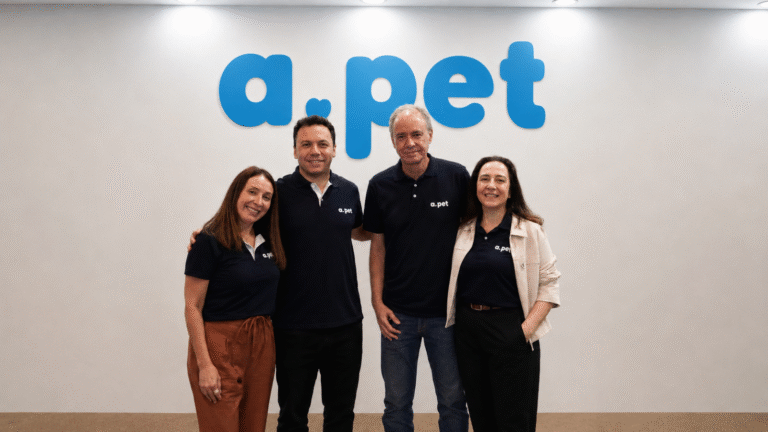 Equipe da APet reunida na sede da empresa, diante da identidade visual da marca.